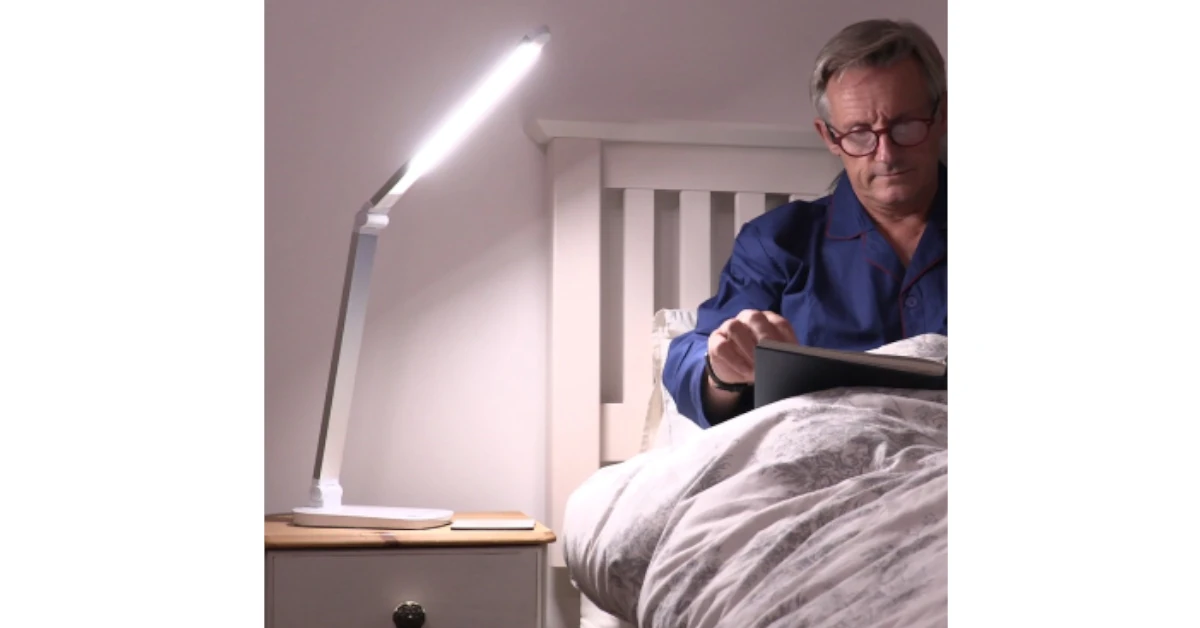 Candeeiro com o braço posicionado a proporcionar uma boa leitura a um senhor que está a ler na cama