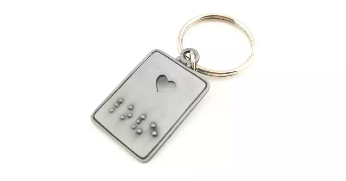 Porta-chaves de metal com argola, um coração perfurado e a inscrição em Braille da palavra LOVE