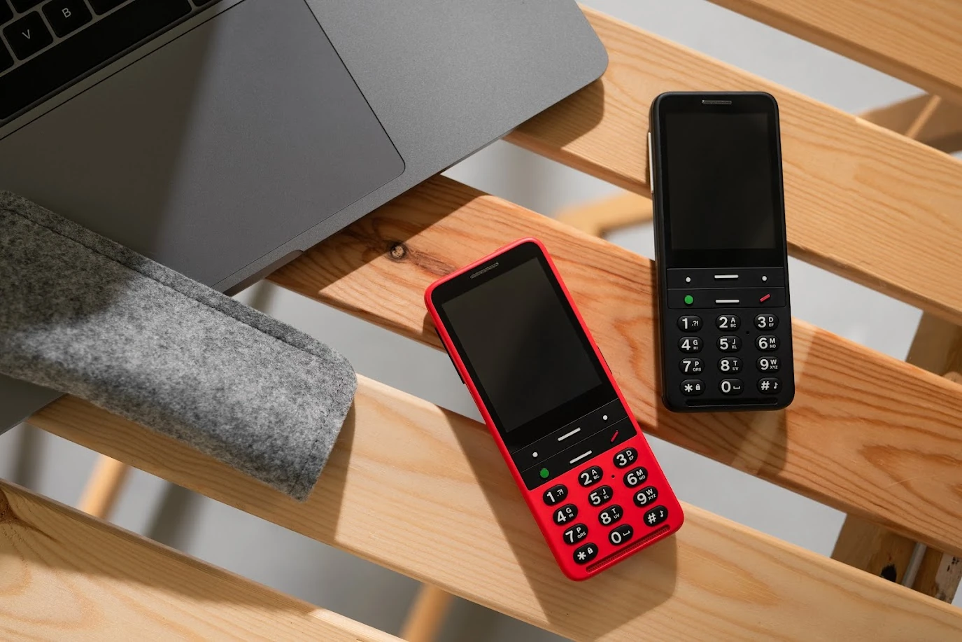 Dois telemóveis BlindShell, um vermelho e outro preto, junto a um computador portátil