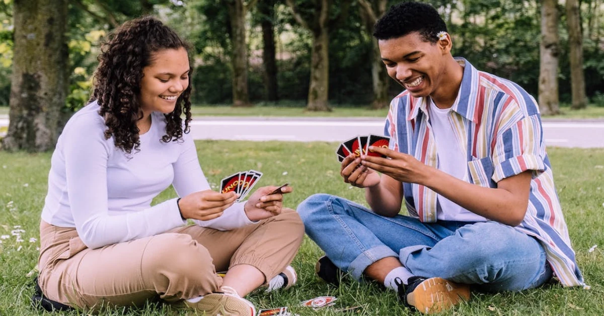 Dois Jovens sentados num jardim divertem-se a jogar o Uno