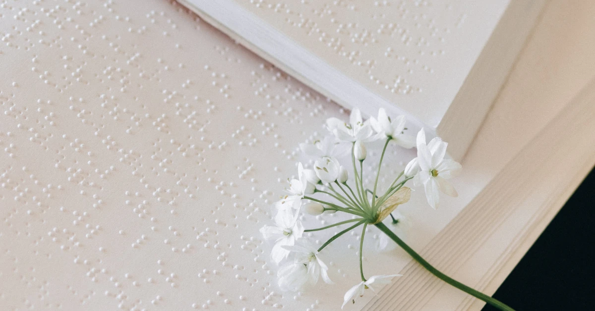 Flor branca pousada em cima de dois livros abertos escritos em Braille