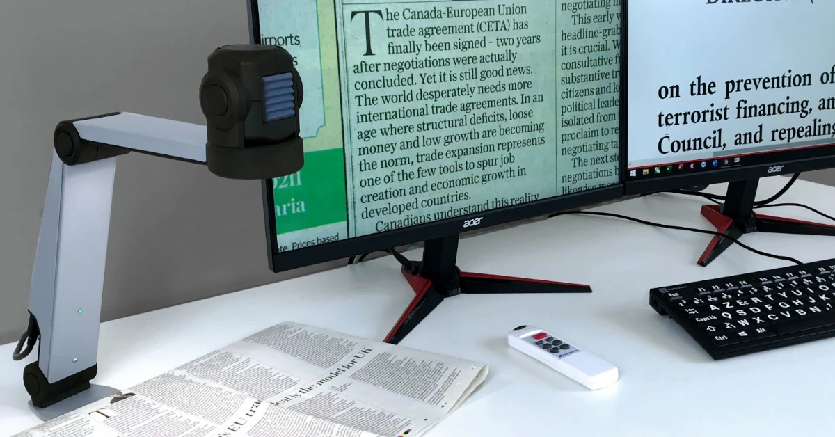 Ampliador de Mesa Koba ZoomCam a ler um jornal, com imagem projetada num ecrã de grande formato
